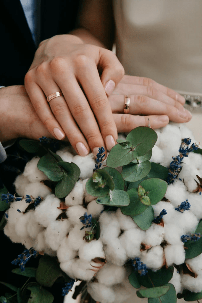 Couple's hands with wedding rings over cotton flowers